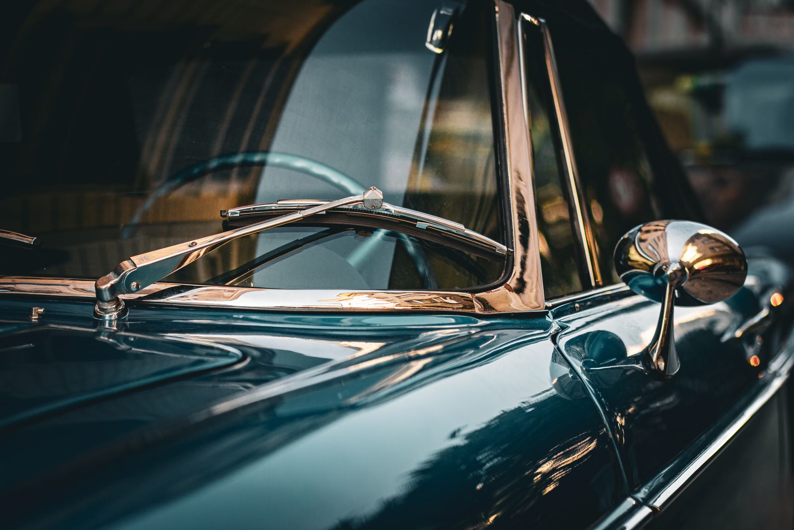 Chrome windscreen trim and mirror of a teal classic car, catching low light