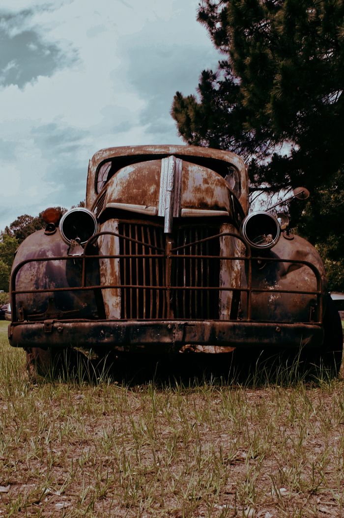 Rusted front grille and headlamps of a pre-war truck standing in a field