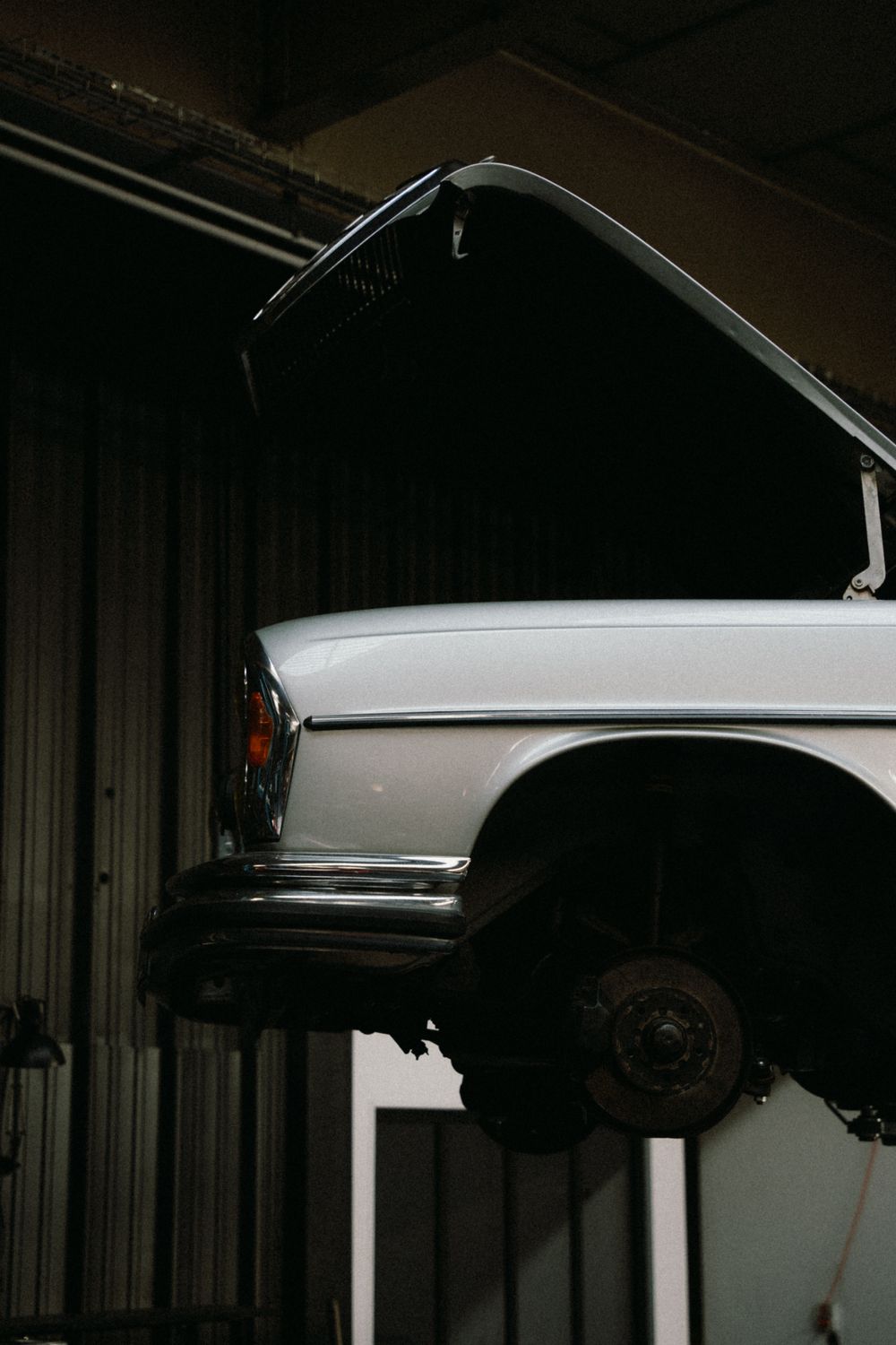 A classic sedan raised on a lift in a dark workshop, hood open